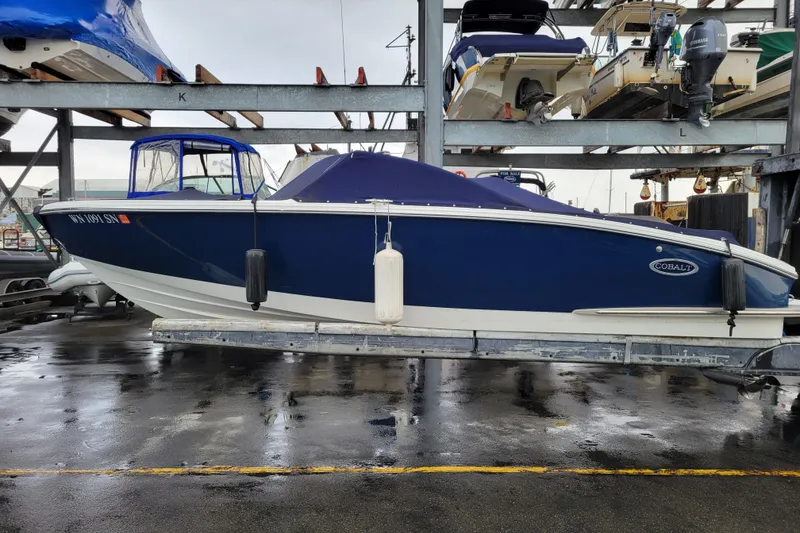 Slide: The Image of 2016 Cobalt CS3 boat in storage, blue hull, covered, on a wet dock. - 26