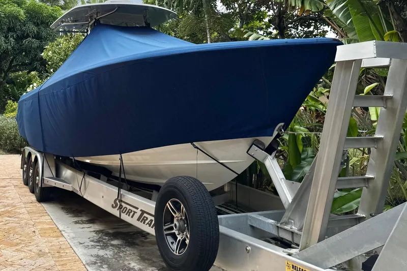 Slide: The Image of 2024 Contender 35 ST boat covered on trailer, surrounded by lush greenery. - 7