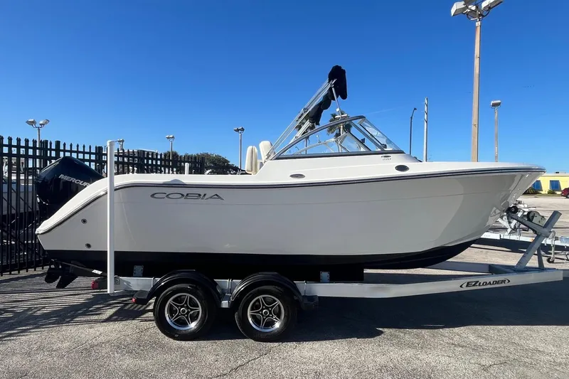 The Image of 2023 Cobia 220 Dual Console boat on trailer, parked outdoors under clear blue sky. - 1