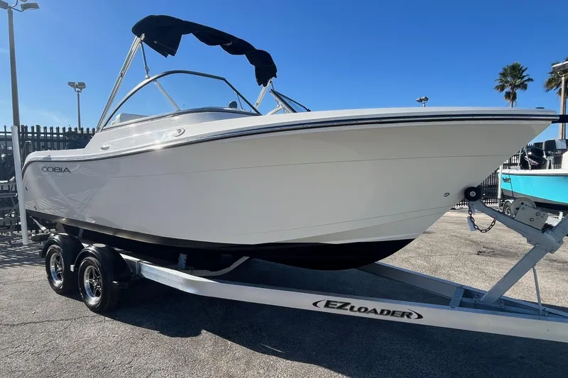 Slide: The Image of 2023 Cobia 220 Dual Console boat on EZ Loader trailer, parked outdoors. - 2