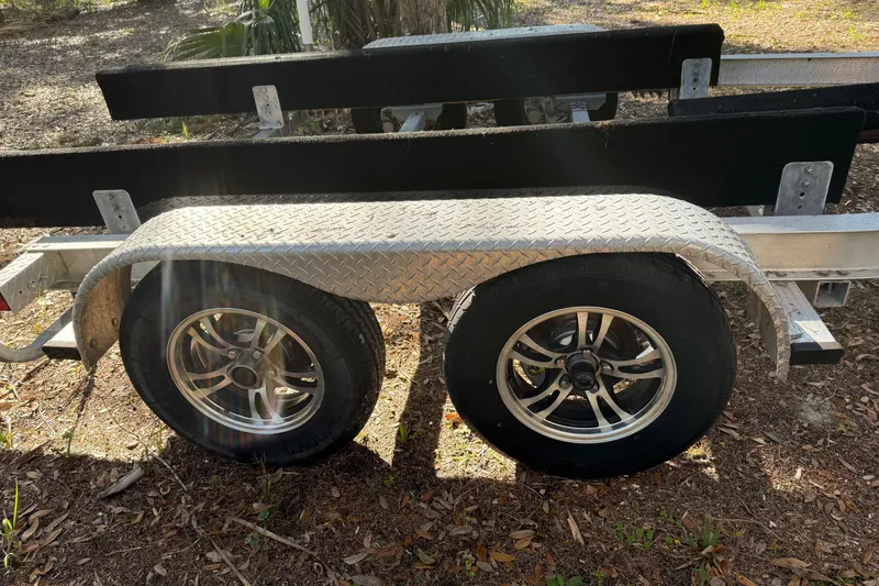 Slide: The Image of Trailer for 2016 Robalo R247 Dual Console boat with dual wheels in a sunny outdoor setting. - 16