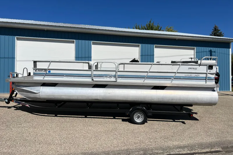 Slide: The Image of 1992 Northwoods Fun Deluxe Pontoon boat on trailer, parked outside blue building. - 2