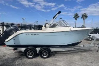 The Image of 2023 Cobia 220 Dual Console boat on trailer, parked outdoors under blue sky. - 1