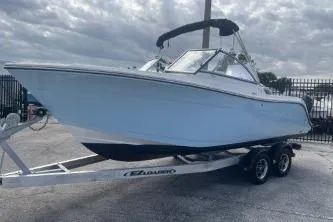 Slide: The Image of 2023 Cobia 220 Dual Console boat on trailer, parked outdoors under cloudy sky. - 4