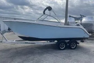 Slide: The Image of 2023 Cobia 220 Dual Console boat on trailer, parked outdoors under cloudy sky. - 5