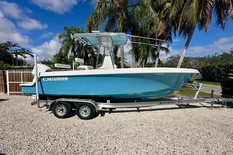 Slide: The Image of 2001 Contender 23 Open boat with V225 engine, parked on gravel, surrounded by palm trees. - 3