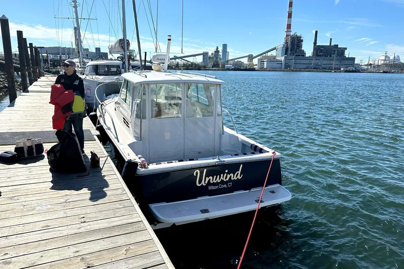 The Image of 2007 Back Cove 29 boat named "Unwind" docked at a marina with industrial backdrop. - 1