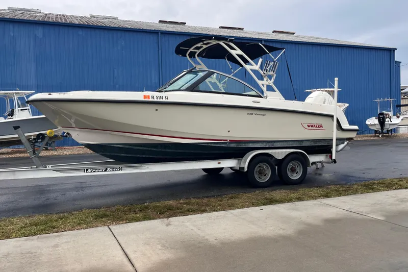 The Image of 2015 Boston Whaler 230 Vantage boat on trailer, parked near blue building. - 0