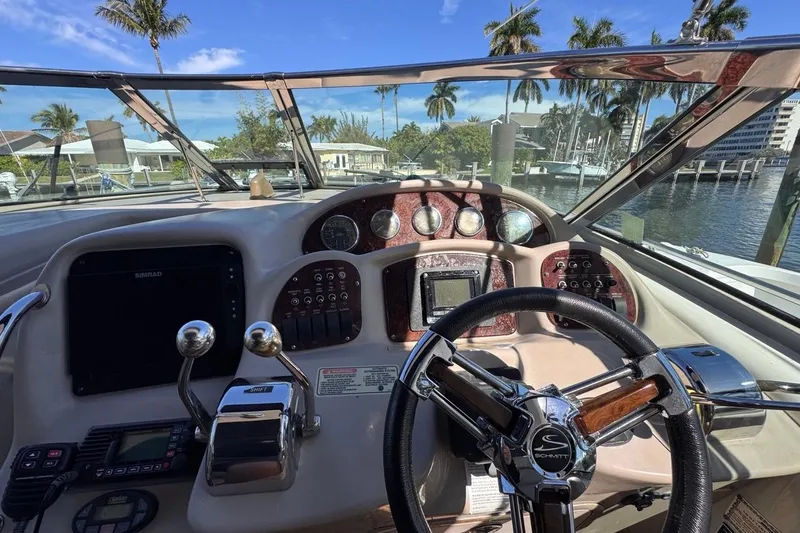Slide: The Image of 2004 Sea Ray 340 Sundancer helm with controls, gauges, and steering wheel, docked by palm trees. - 33