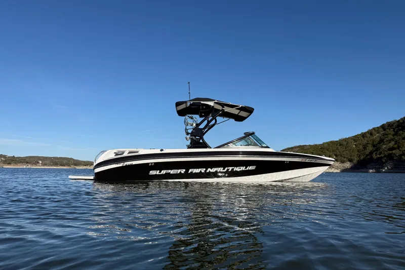 Slide: The Image of 2010 Nautique Super Air Nautique 210 boat on a calm lake under clear blue sky. - 6