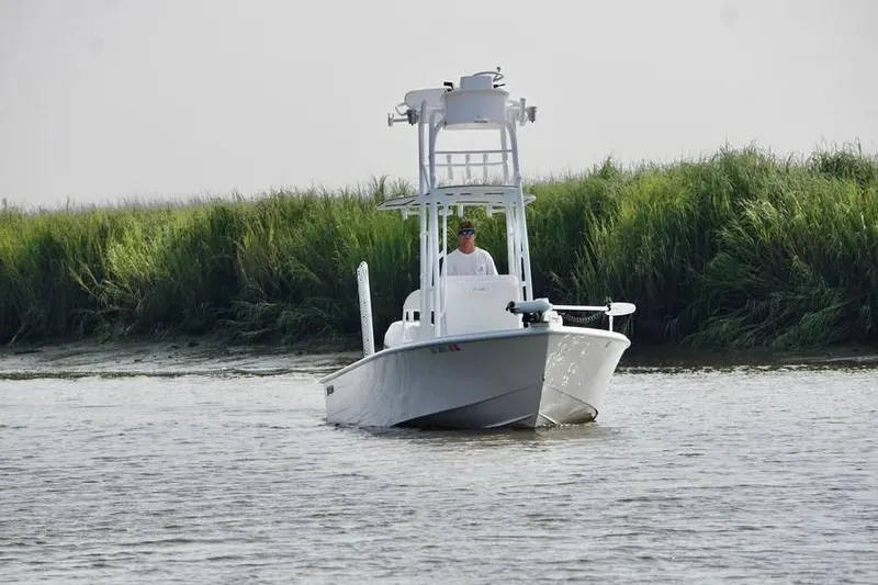 Slide: The Image of 2021 Dorado Flatdeck boat navigating a calm river near grassy shoreline. - 2