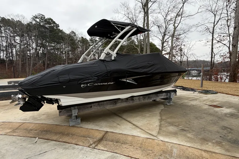 Slide: The Image of 2022 Crownline 240 SS boat covered, parked on a concrete surface near a wooded area. - 2