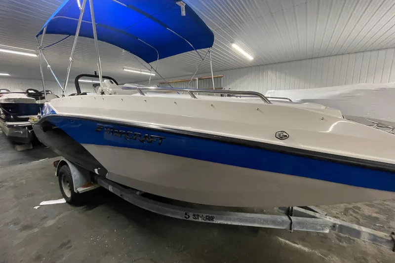 The Image of 2026 Starcraft SVX 191 OB boat with blue canopy in indoor storage. - 1