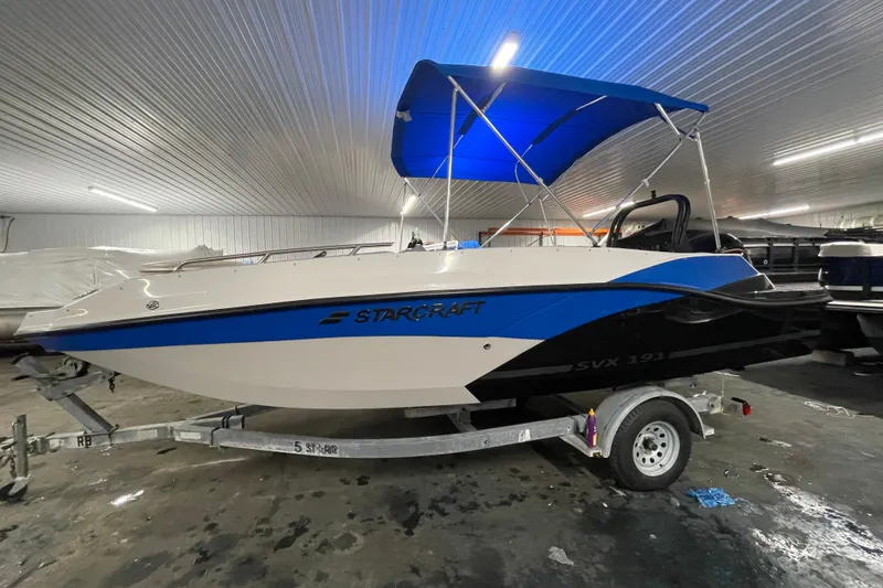 Slide: The Image of 2026 Starcraft SVX 191 OB boat with blue canopy in indoor storage. - 6