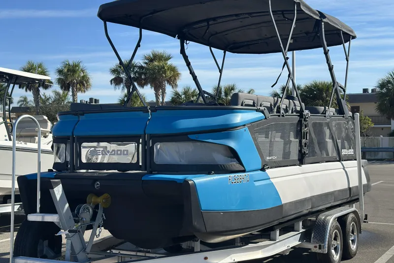 Slide: The Image of 2022 Sea-Doo Switch Sport 21 pontoon boat on trailer, parked with palm trees in background. - 5