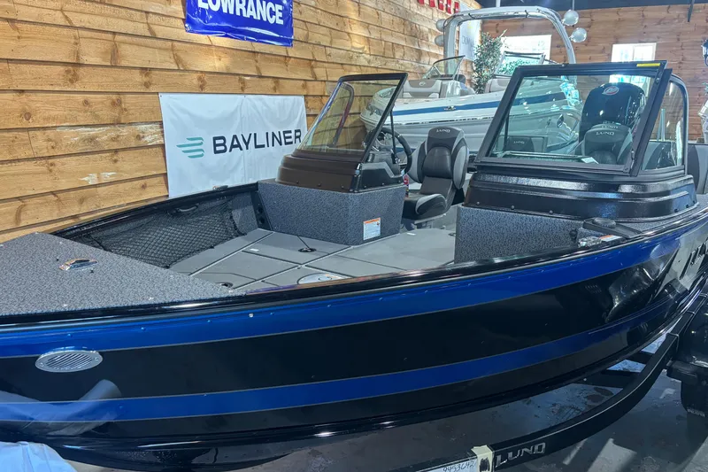 The Image of 2026 Lund 1875 Impact XS boat displayed indoors, featuring sleek design and modern seating. - 1