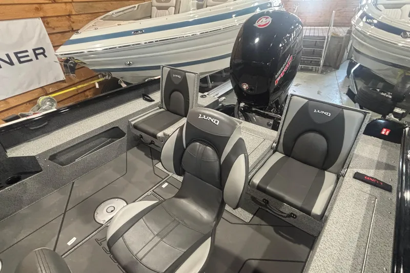 Slide: The Image of 2026 Lund 1875 Impact XS boat interior with seating and motor in showroom. - 10