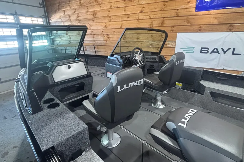 Slide: The Image of 2026 Lund 1875 Impact XS boat interior with seating and dashboard in a wooden garage. - 4