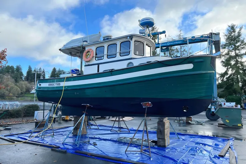 Slide: The Image of 1981 Nordic Tug Cricket boat on dry dock, vibrant green hull, clear sky background. - 69