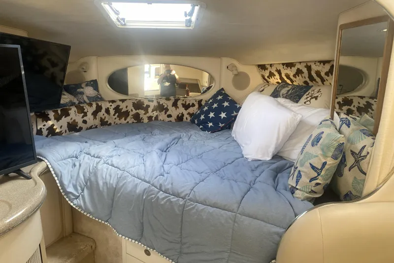 Slide: The Image of 1998 Searay Sundancer cabin interior with cozy bed, nautical-themed pillows, and natural light. - 4