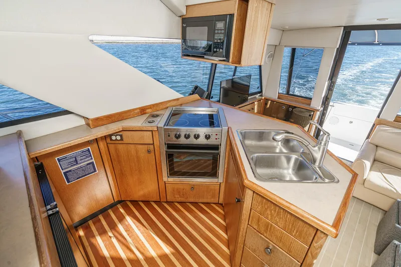 Slide: The Image of 1998 Bayliner 3988 Motoryacht kitchen with stove, sink, and wooden cabinetry, overlooking the water. - 34