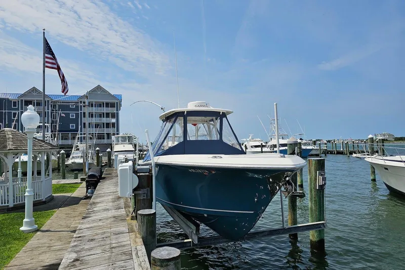 Slide: The Image of 2014 Sailfish 290 CC boat docked at marina with American flag and waterfront buildings. - 12