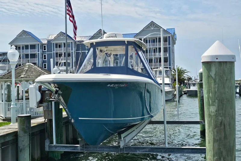 Slide: The Image of 2014 Sailfish 290 CC boat docked at marina with American flag and waterfront buildings. - 2