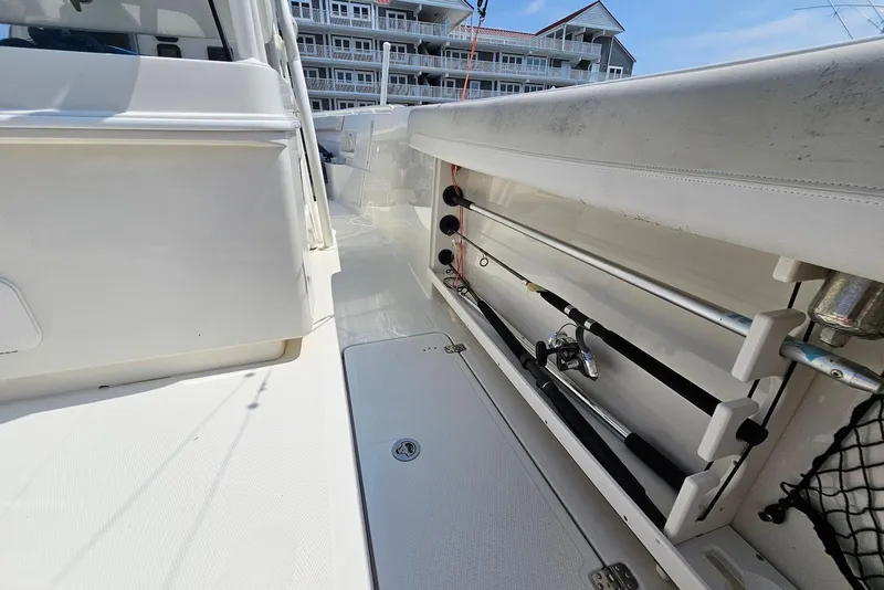 Slide: The Image of 2014 Sailfish 290 CC boat interior with fishing rod holders and residential backdrop. - 21