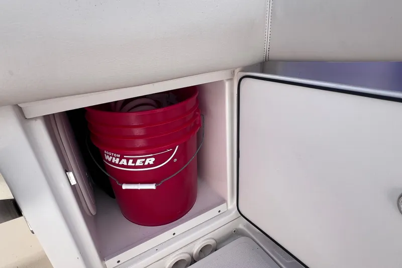 Slide: The Image of Red Boston Whaler bucket stored in a compartment of a 2021 Boston Whaler 330 Outrage boat. - 22
