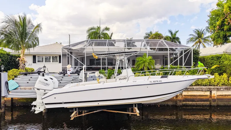 The Image of Century 2600 CC boat from 1999 docked by a waterfront home with lush greenery. - 0