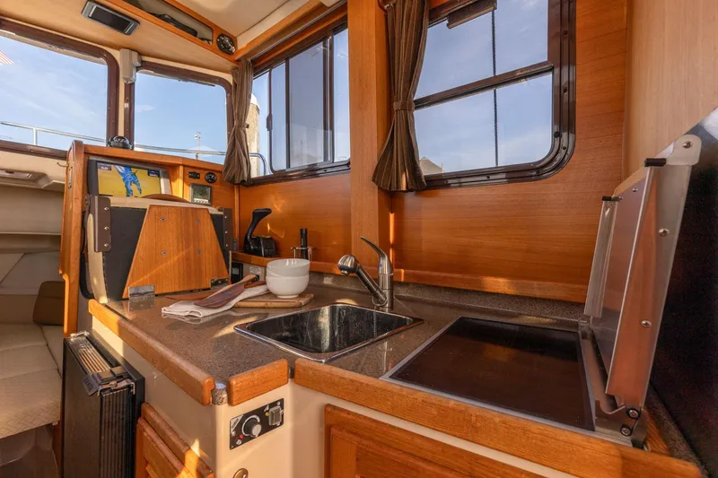 Slide: The Image of 2012 Ranger Tugs R-25 SC interior with kitchenette, featuring sink, stove, and wooden cabinetry. - 12