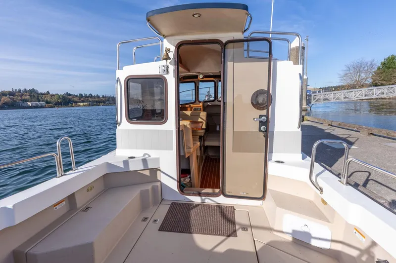 Slide: The Image of 2012 Ranger Tugs R-25 SC boat interior with open cabin door, docked by a scenic lake. - 5
