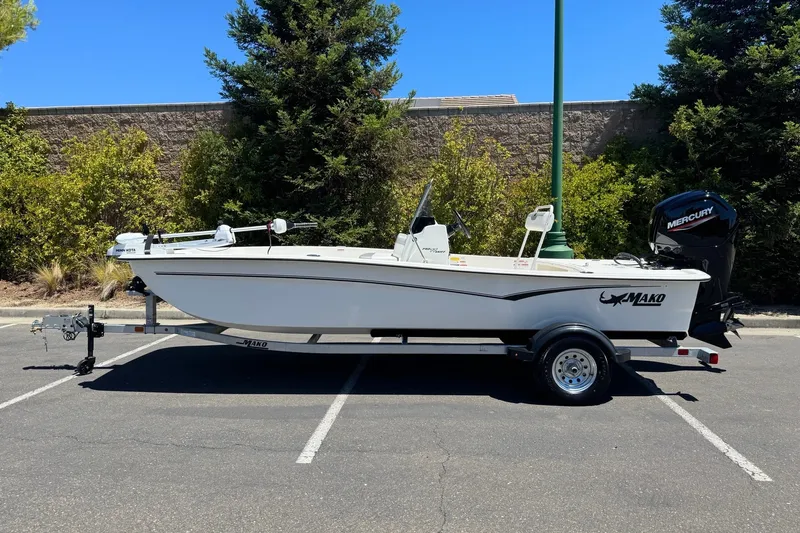 The Image of 2026 Mako Pro Skiff 17 CC boat on trailer in parking lot, surrounded by trees. - 0