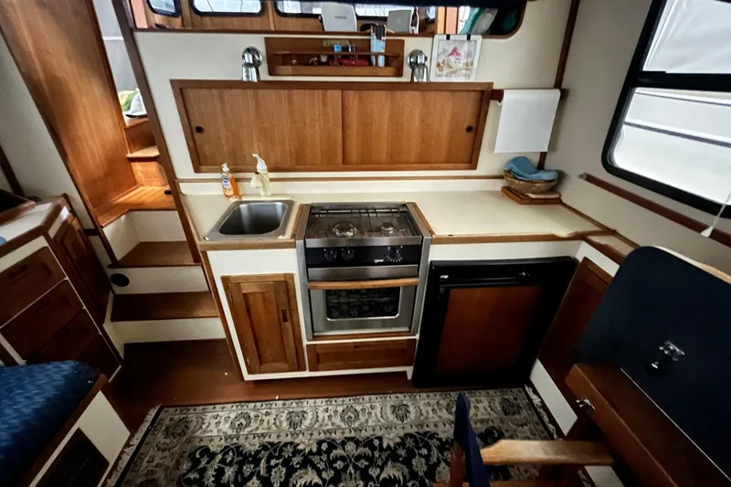 Slide: The Image of 1999 Nordic Tug 32 interior kitchen with wooden cabinetry, sink, stove, and compact refrigerator. - 10