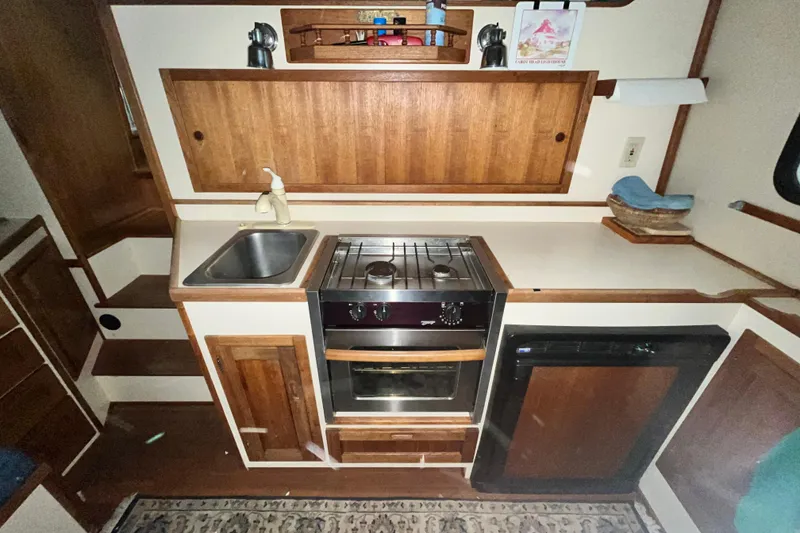 Slide: The Image of 1999 Nordic Tug 32 galley with stove, sink, and wooden cabinetry. - 11
