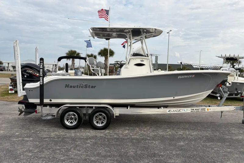 Slide: The Image of 2022 NauticStar 2302 Legacy boat on trailer, displayed outdoors with flags. - 5