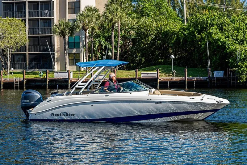 Slide: The Image of 2019 NauticStar 243DC Sport Deck boat cruising on a sunny day near waterfront homes. - 25
