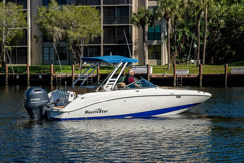 Slide: The Image of 2019 NauticStar 243DC Sport Deck boat cruising on a sunny day near waterfront buildings. - 27