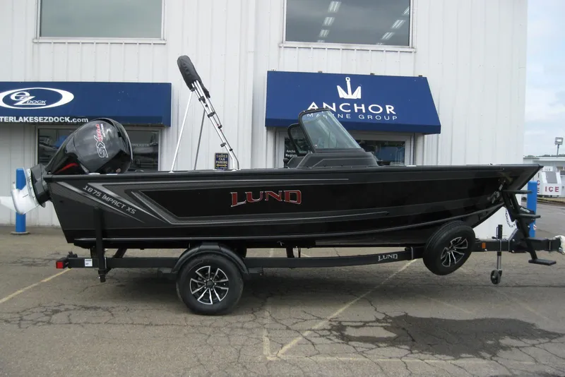 Slide: The Image of 2025 Lund 1875 Impact XS Sport boat on trailer outside marine store. - 1
