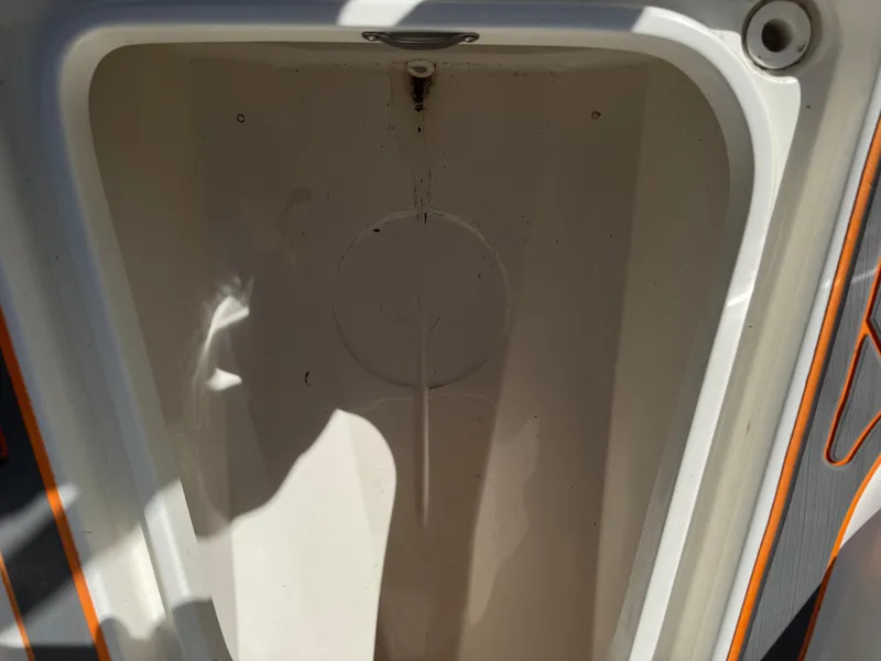 Slide: The Image of Empty storage compartment in a 2019 Mako 214C boat, with visible shadows and orange trim. - 42