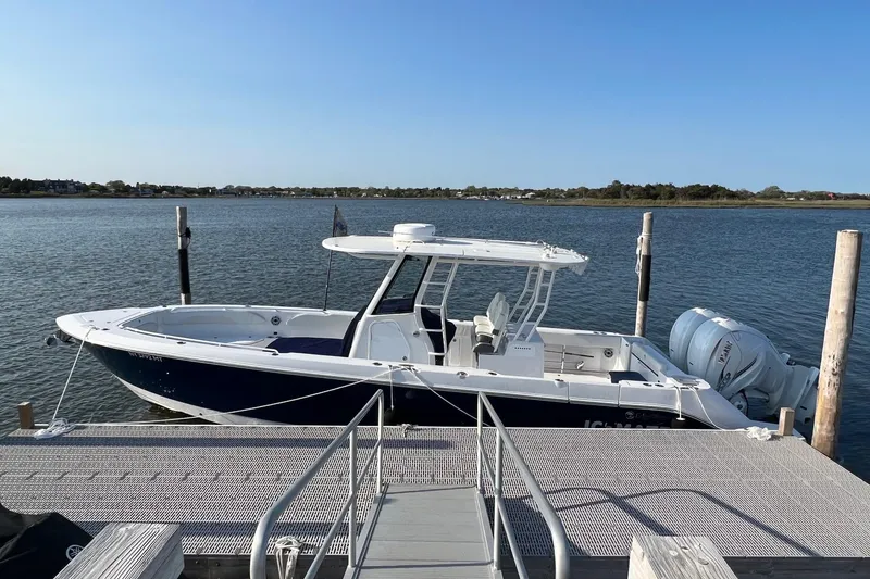 Slide: The Image of 2023 Edgewater 340CC boat docked on a calm lake under clear blue skies. - 1