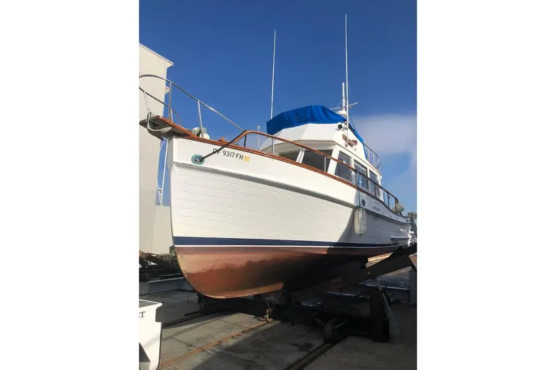Slide: The Image of 1973 Grand Banks 32 Sedan boat on dry dock, white hull, blue cover, clear sky. - 46