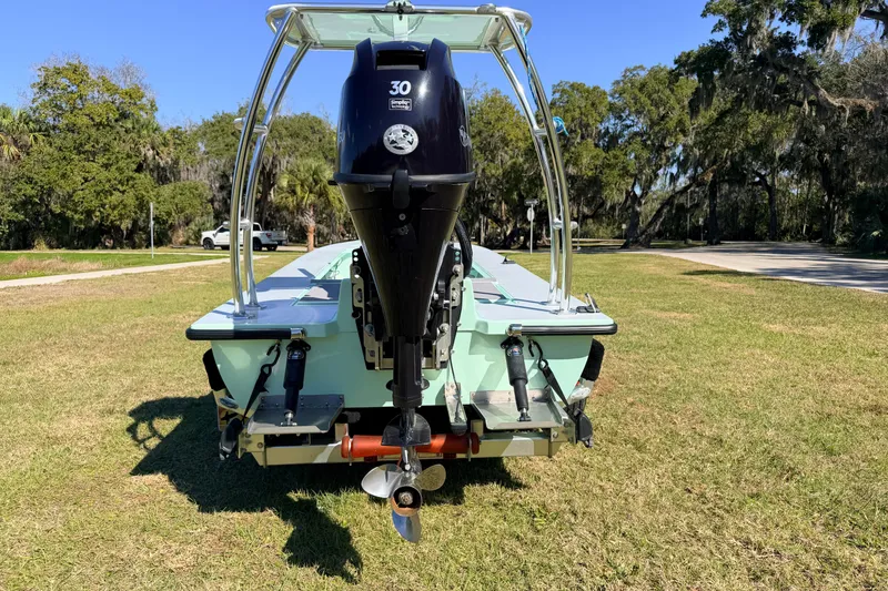 Slide: The Image of 2011 Hell's Bay Glades Skiff with outboard motor on grassy area, surrounded by trees. - 3