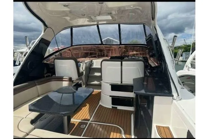 Slide: The Image of 2016 Searay Sundancer 370 Gen 3 interior with seating, table, and helm, docked under cloudy skies. - 5