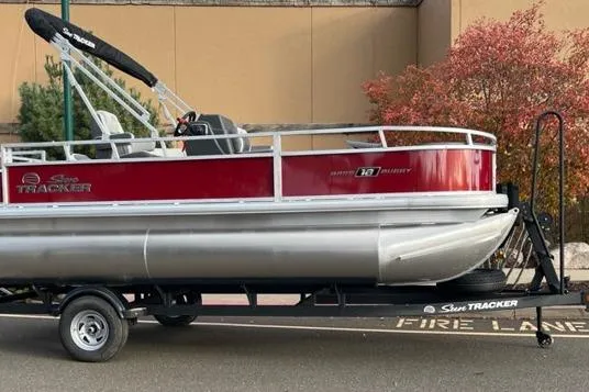 The Image of 2026 Sun Tracker Bass Buggy 18 DLX pontoon boat on trailer, parked near autumn foliage. - 0