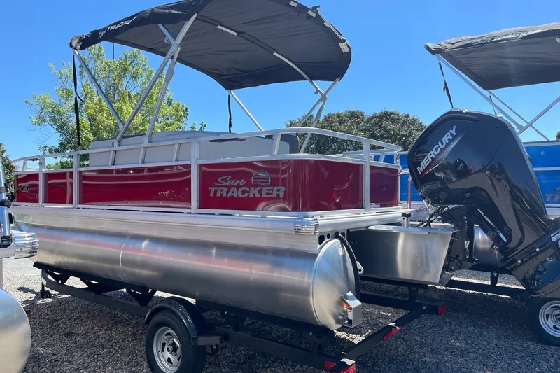 Slide: The Image of 2026 Sun Tracker Bass Buggy 18 DLX pontoon boat with Mercury engine, parked outdoors. - 2