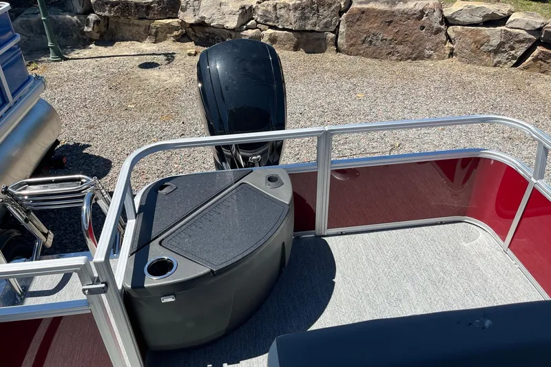 Slide: The Image of 2026 Sun Tracker Bass Buggy 18 DLX pontoon boat with outboard motor, docked on gravel. - 5