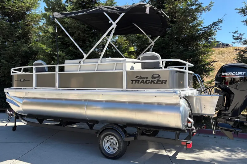 Slide: The Image of 2026 Sun Tracker Bass Buggy 18 DLX pontoon boat with Mercury engine, parked outdoors. - 9