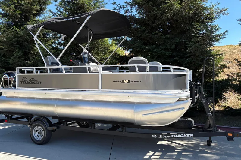 Slide: The Image of 2026 Sun Tracker Bass Buggy 18 DLX pontoon boat on trailer, parked outdoors. - 2