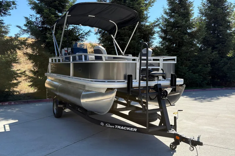 Slide: The Image of 2026 Sun Tracker Bass Buggy 18 DLX pontoon boat on trailer, parked outdoors. - 5